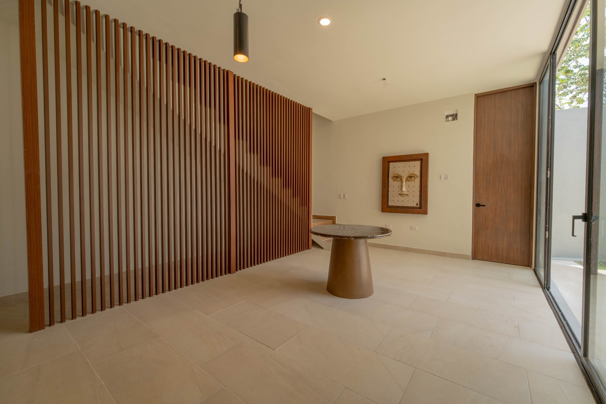 Sala con pared de listones de madera, mesa redonda, cuadro y puerta de madera.