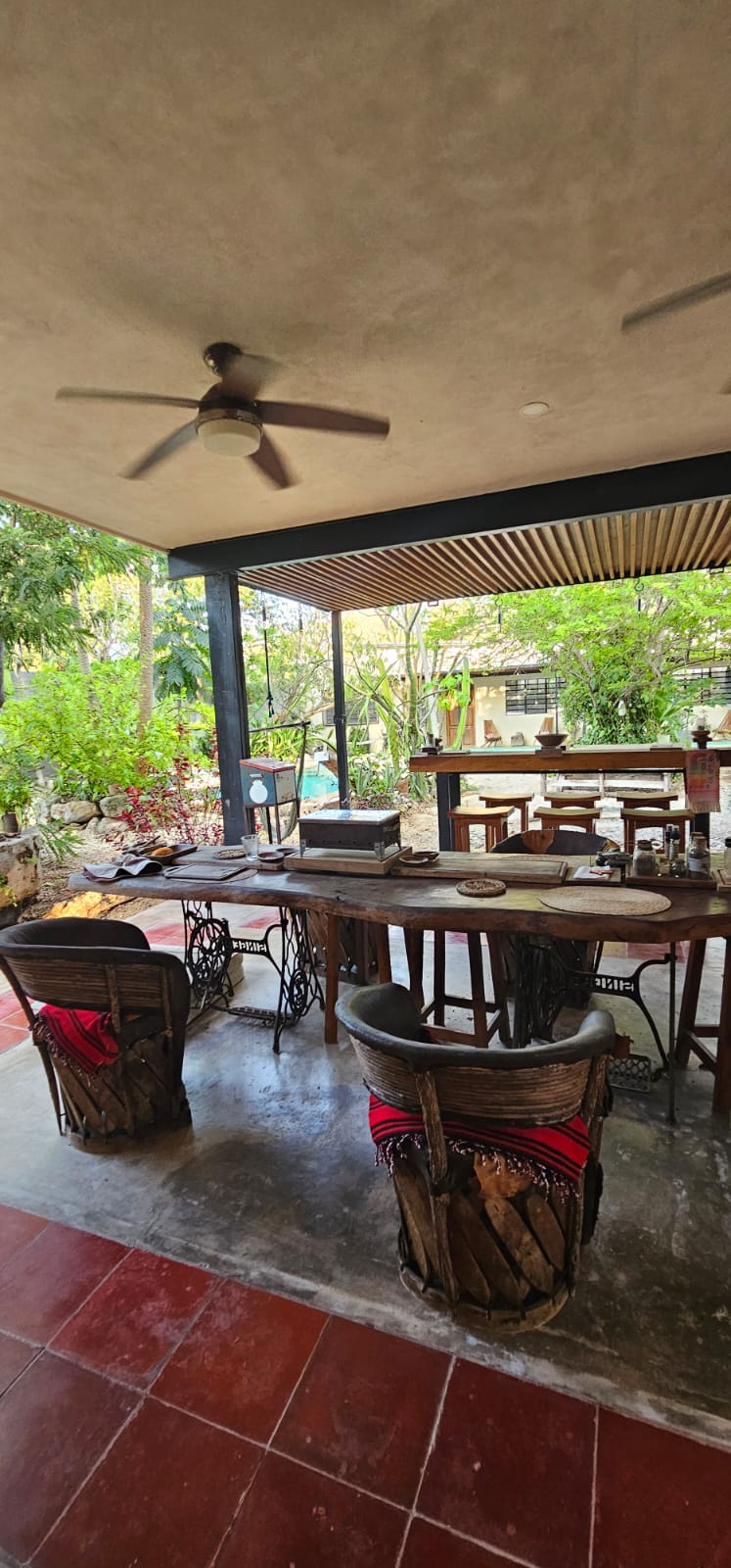 Comedor exterior con mesa de madera rústica, sillas de madera y ventilador de techo.
