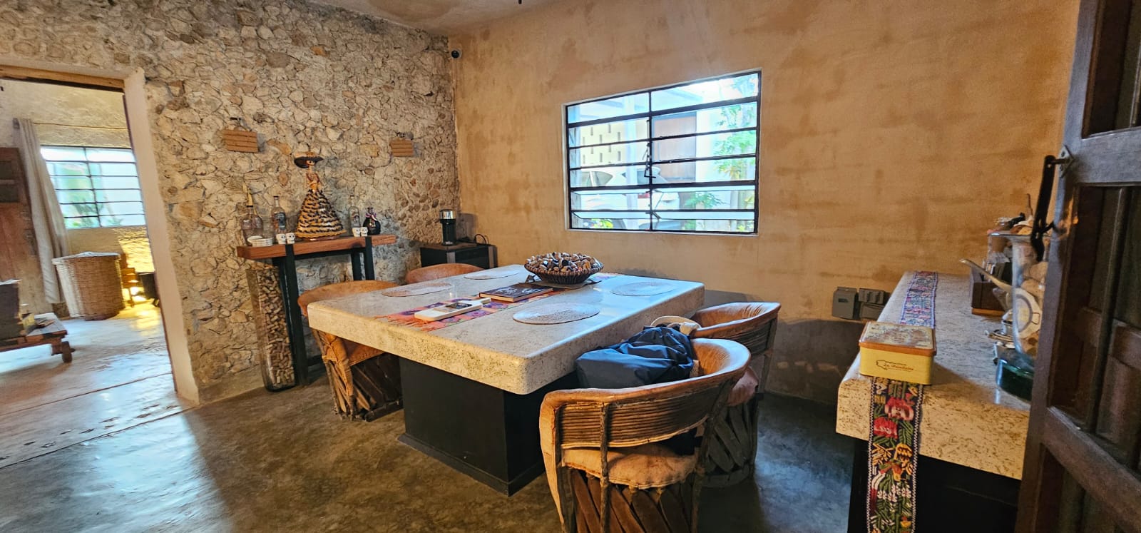 Comedor rústico con mesa de piedra, sillas de madera y paredes de piedra y estuco.
