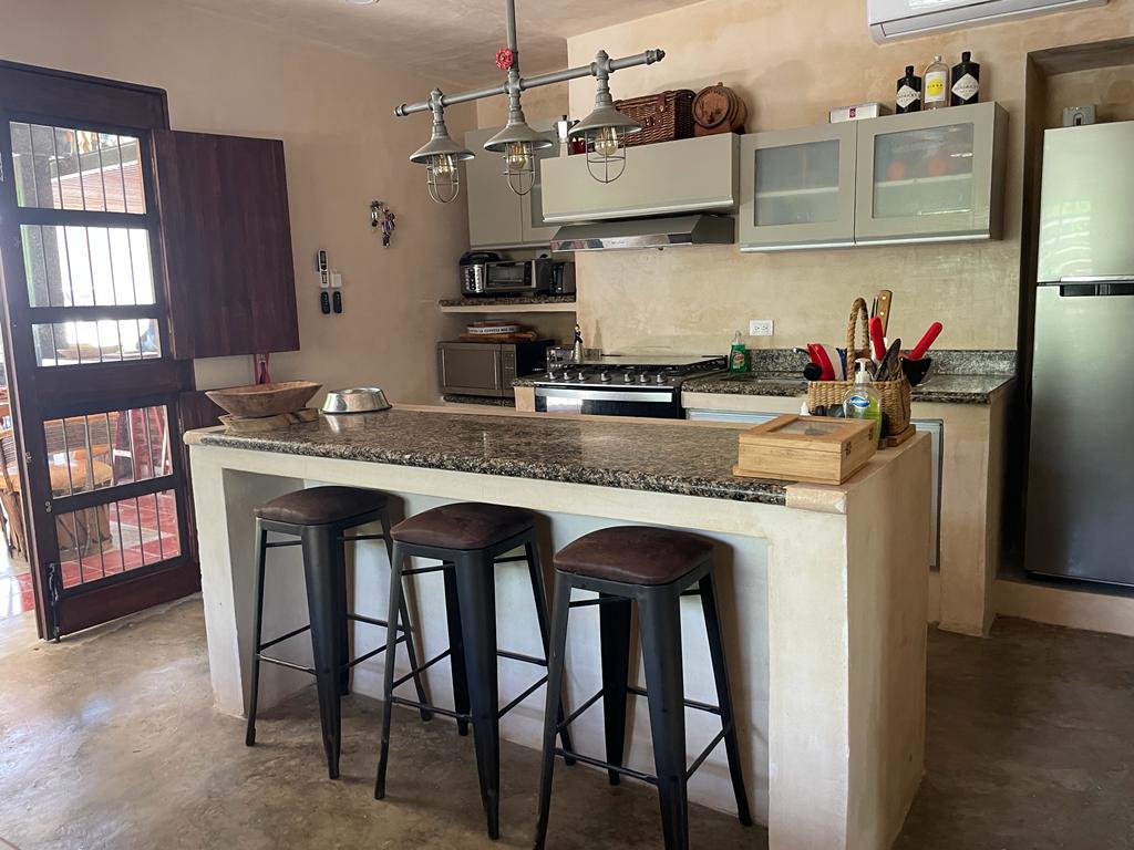 Cocina con barra de granito, taburetes, estufa, refrigerador y gabinetes superiores.