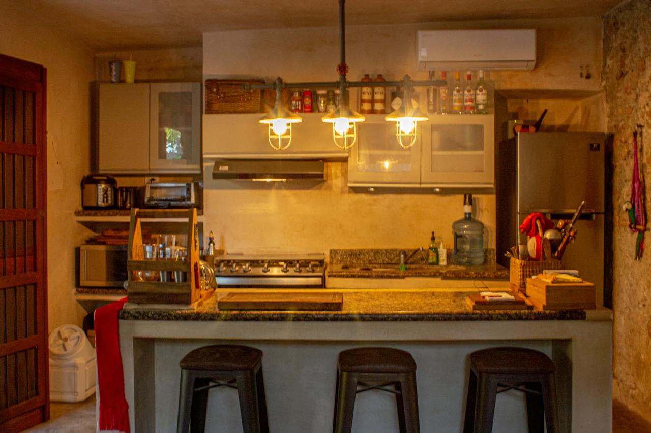 Cocina con barra, taburetes, estufa, refrigerador y gabinetes superiores e inferiores.