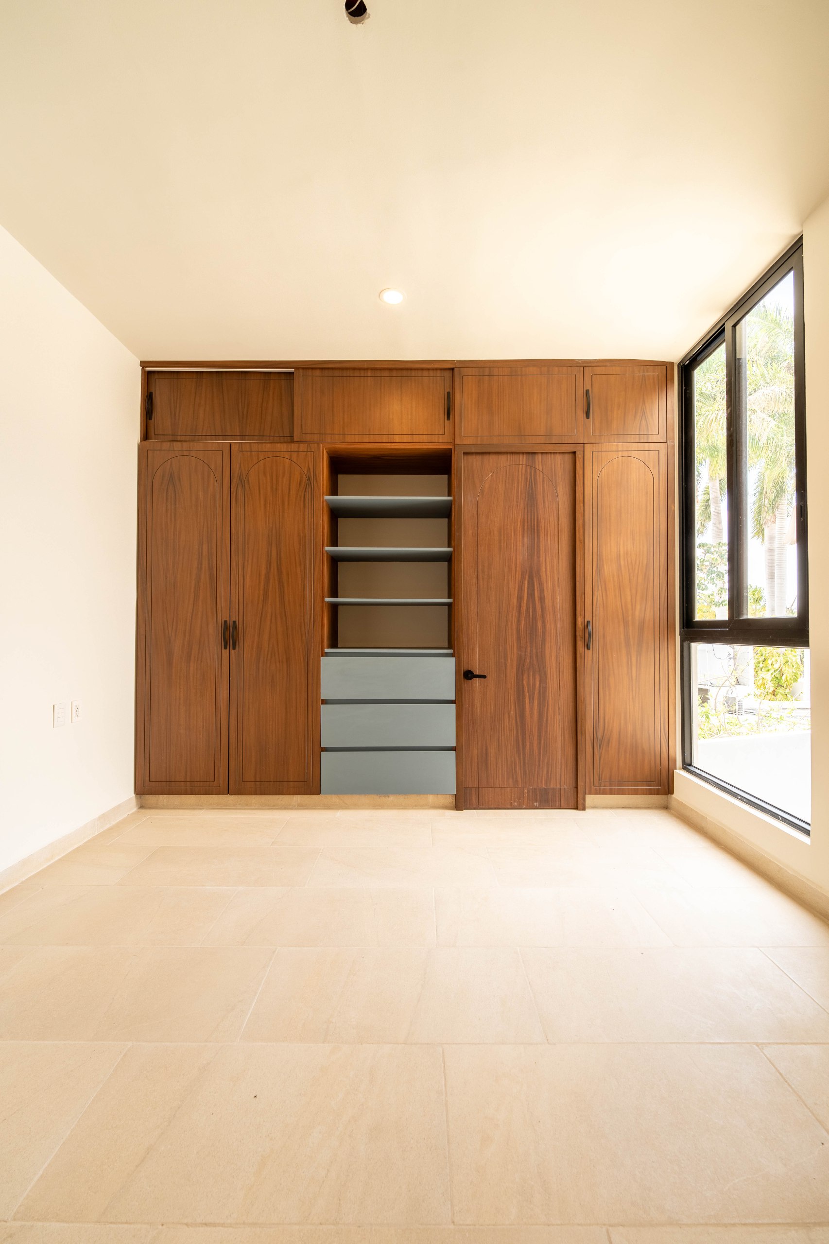 Habitación con armario de madera empotrado, estantes y cajones, junto a una ventana grande.