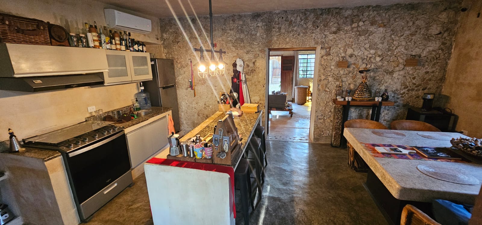 Cocina rústica con paredes de piedra, estufa, refrigerador, barra y mesa de comedor.