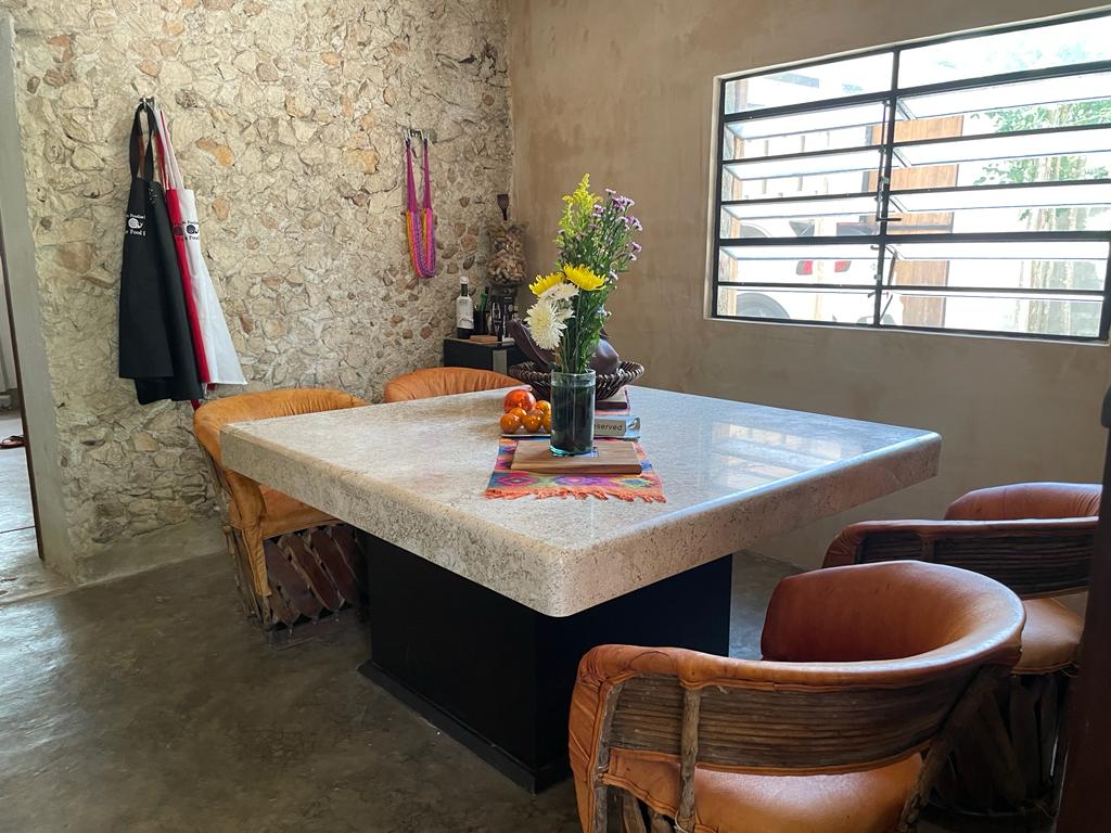 Comedor rústico con mesa de granito, sillas de cuero y pared de piedra.