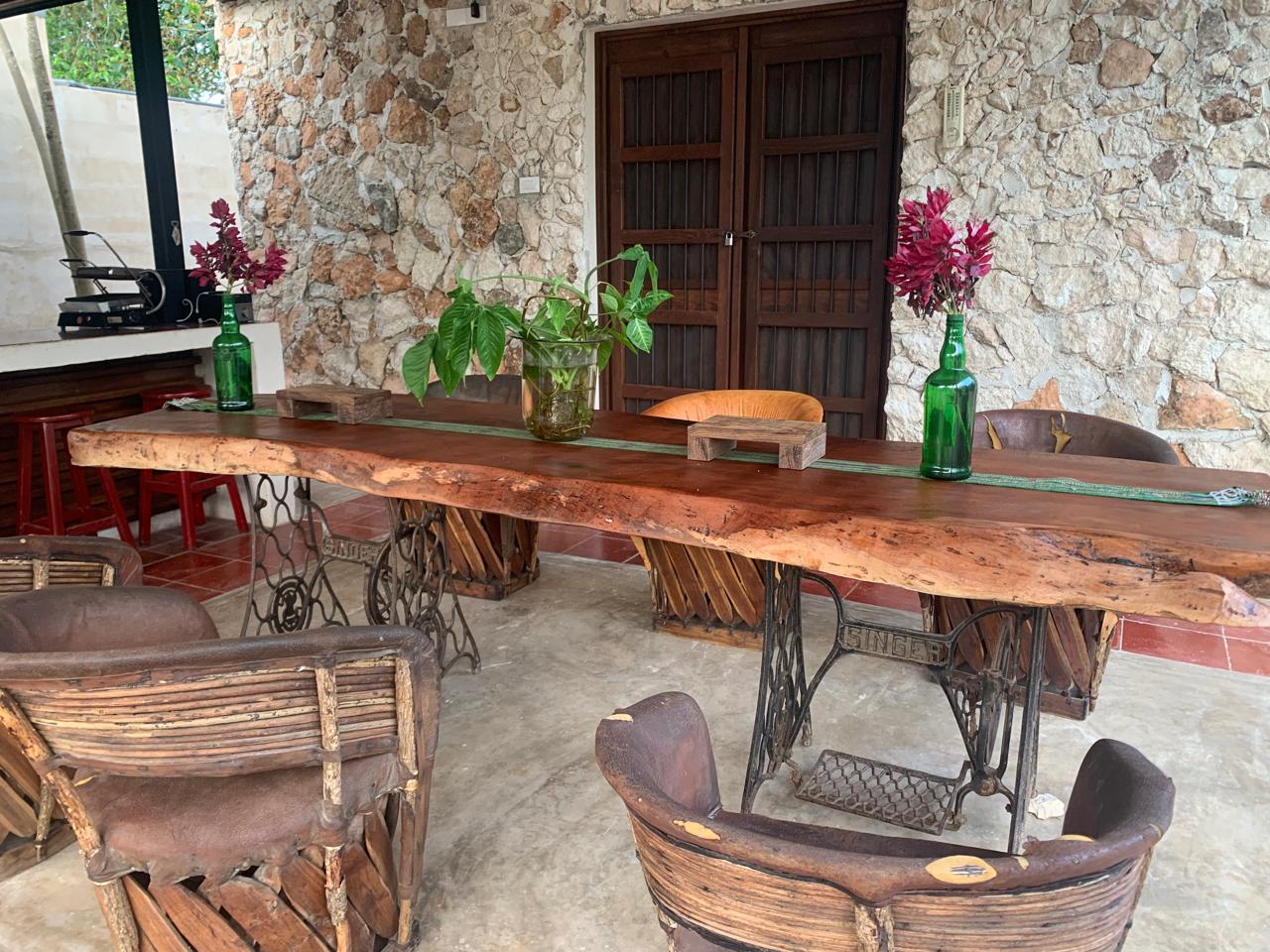 Mesa de madera rústica con base de máquina de coser y sillas de mimbre en comedor exterior.