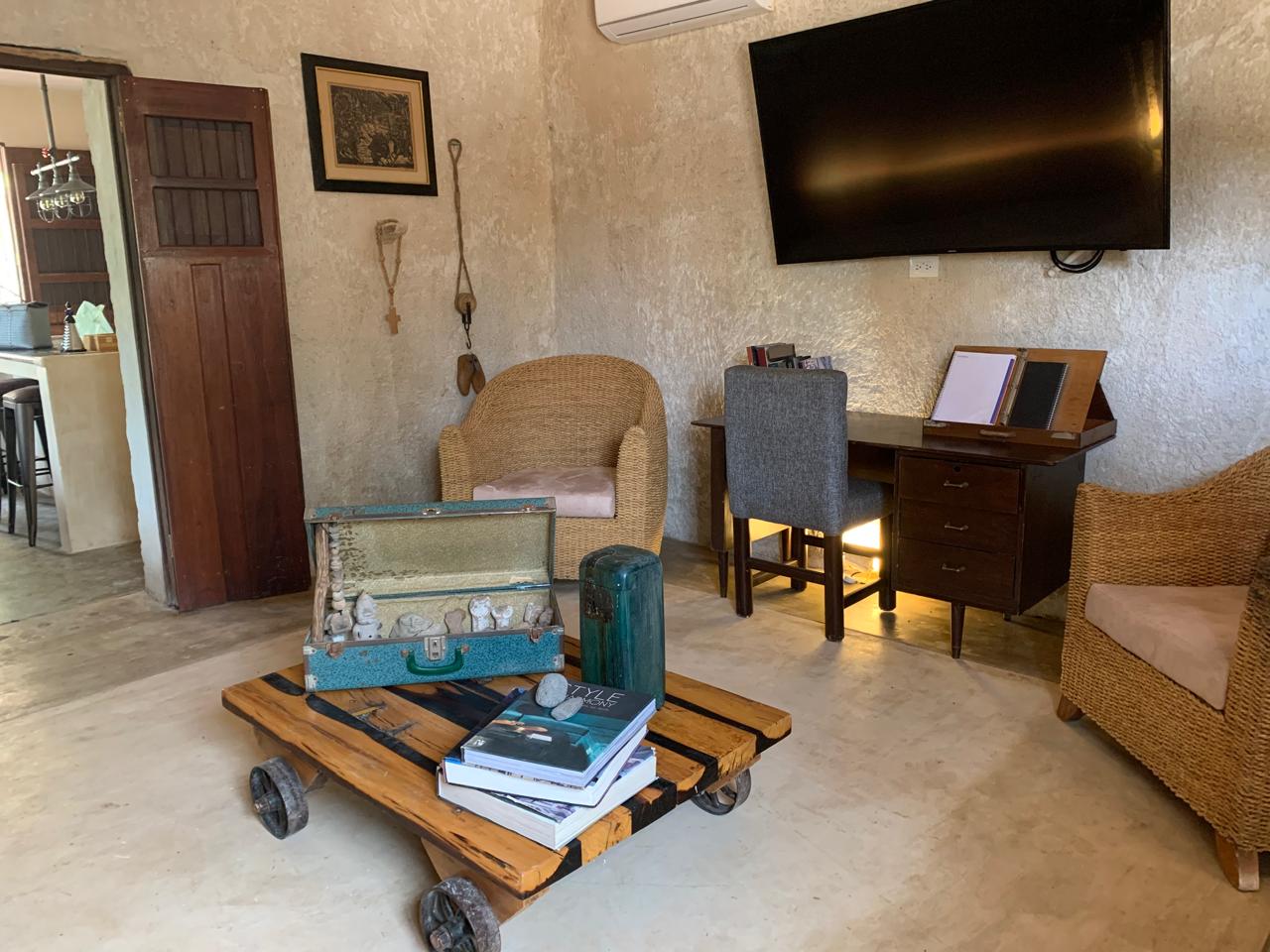 Sala con sillones de mimbre, escritorio de madera, televisión y mesa de centro rústica.
