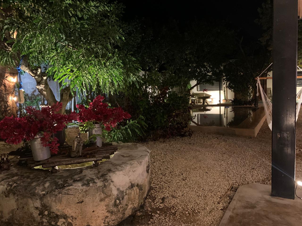 Patio exterior con gravilla, plantas, una hamaca y una pequeña piscina iluminada por la noche.